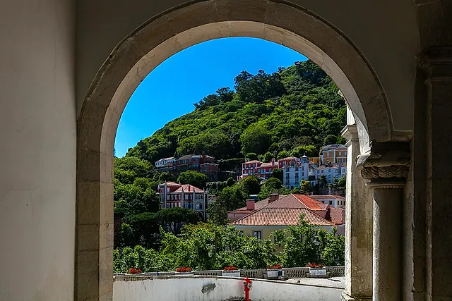 Uitzicht door een stenen boog van het Nationaal Paleis van Sintra naar de beboste heuvel van het Moorse Kasteel