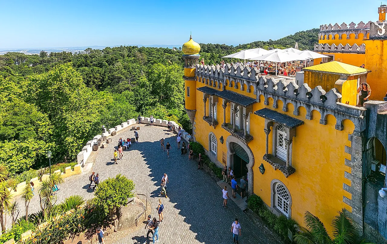 Het gele terras van het Paleis van Pena met kantelen en bogen boven de groene heuvels van Sintra
