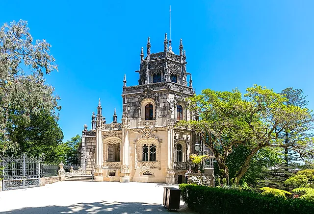 Het neo-Manuelijnse paleis van Regaleira omlijst door bomen onder een blauwe hemel